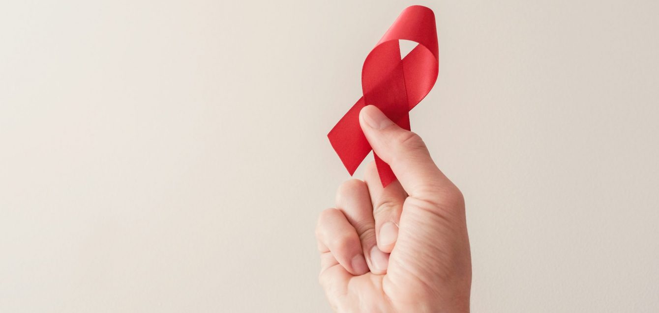 Hand holding red ribbon on red background, hiv awareness concept