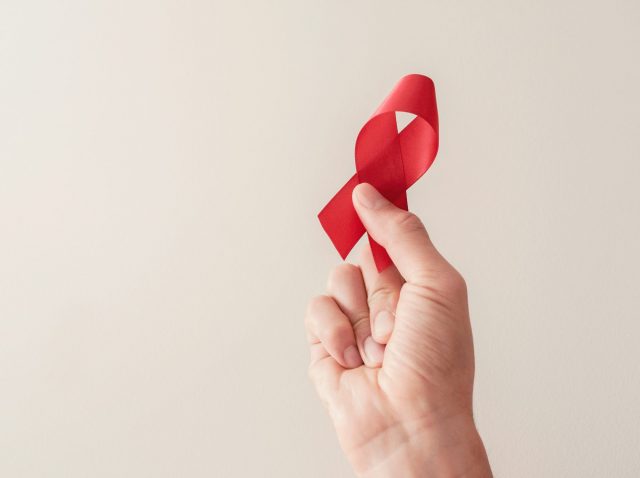 Hand holding red ribbon on red background, hiv awareness concept Hand holding red ribbon on red background, hiv awareness concept
