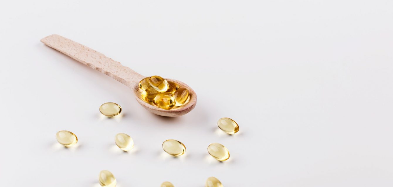 Oil capsule for hair with vitamin E lie on wooden spoon