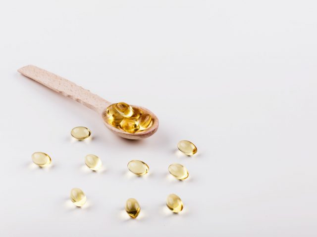 Oil capsule for hair with vitamin E lie on wooden spoon Oil capsule for hair with vitamin E lie on wooden spoon