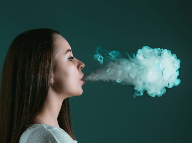 The face of vaping young woman at black studio The face of vaping young woman at black studio