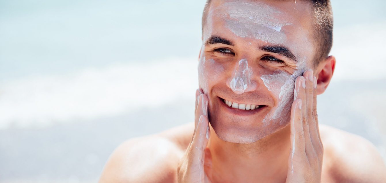 Cheerful man puts the lotion on face to protect a skin, on the beach Cheerful man puts the lotion on face to protect a skin, on the beach
