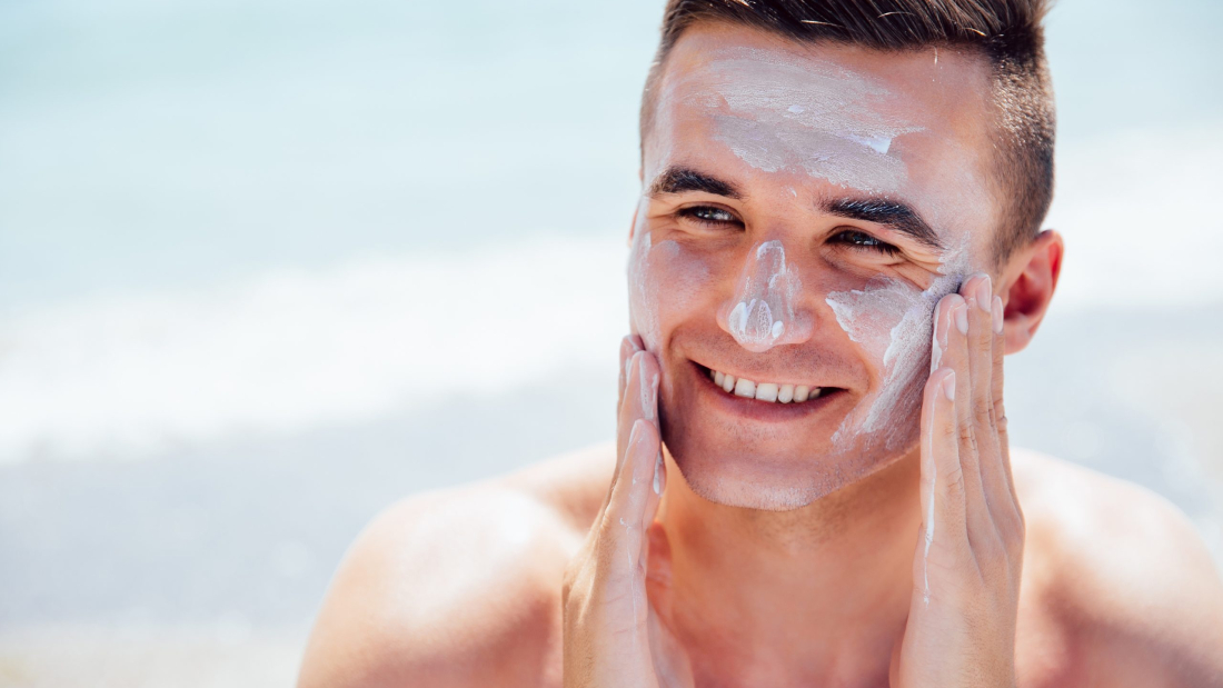 Hombre sonriente poniéndose crema bronceadora en la cara, toma el sol en la playa. Atención sanitaria.