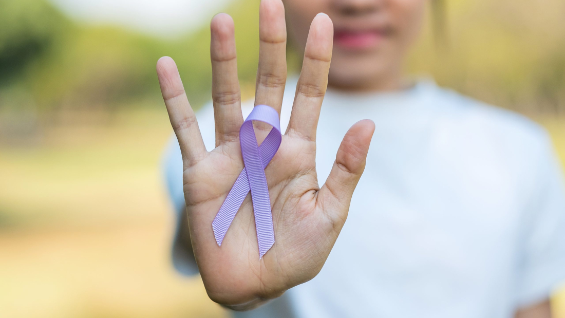 Día mundial contra el cáncer (4 de febrero). Mano de mujer que sostiene un lazo violeta lavanda para apoyar a las personas que viven con la enfermedad. Concepto médico y sanitario