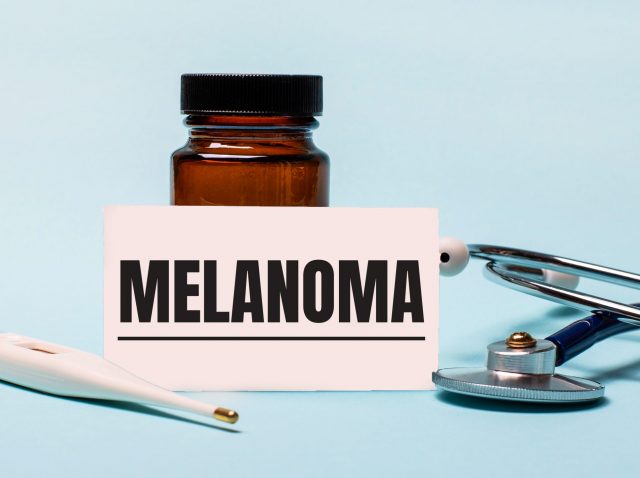 On a blue background - a bottle for pills, a stethoscope, an electronic thermometer and a card with the inscription MELANOMA. Medical concept