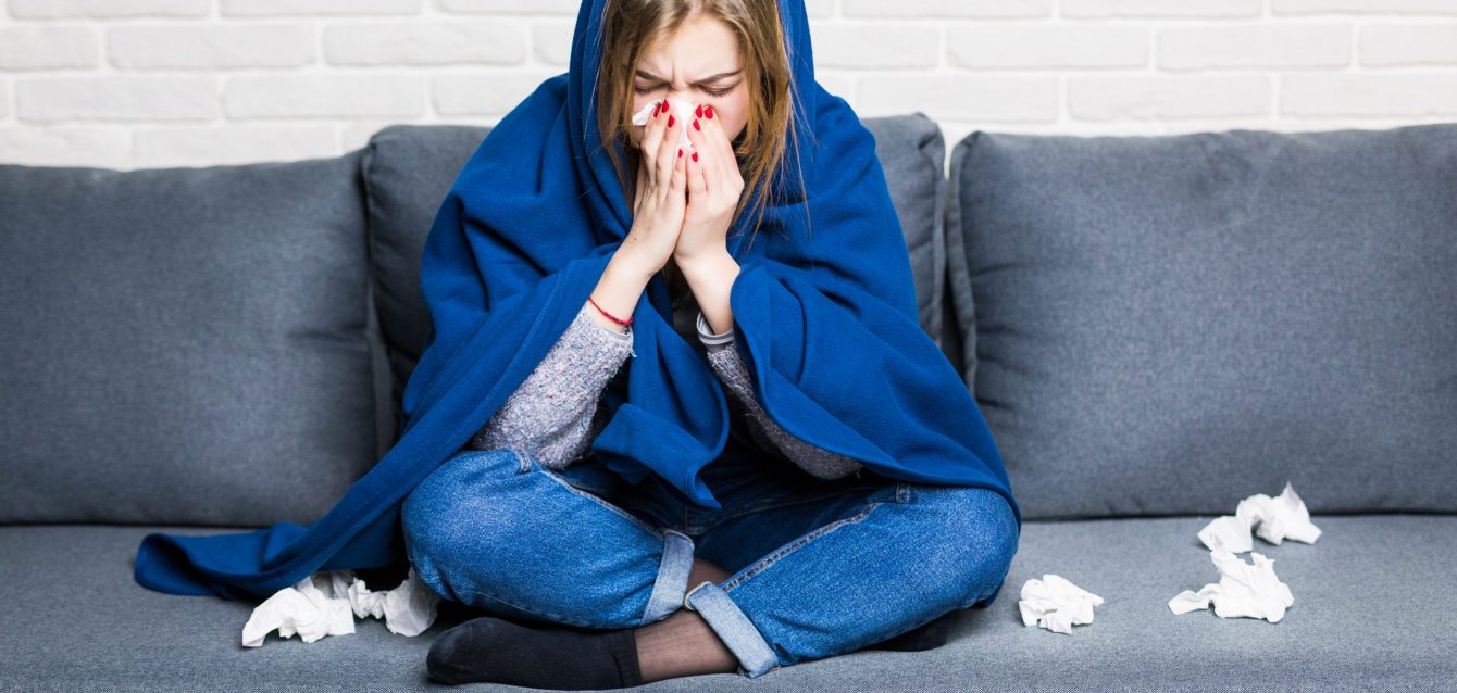 Sick woman with rheum and headache holding napkin, sitting on sofa with coveret and pills at home Sick woman with rheum and headache holding napkin, sitting on sofa with coveret and pills at home