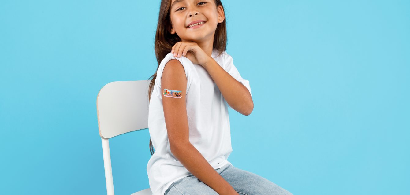 Niña feliz vacunada mostrando el brazo después de la vacunación, fondo azul