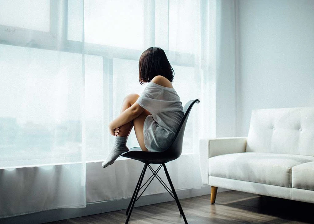 Foto de la Depresión Joven sentada en una silla mirando por la ventana